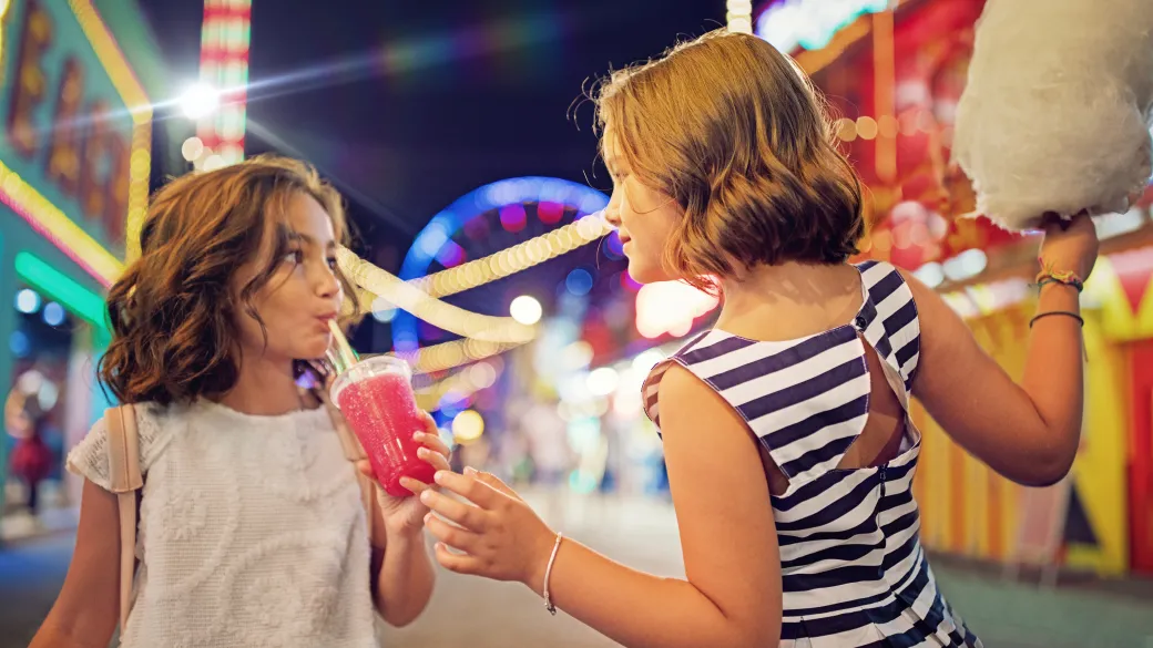 two young girls at a fair sharing a cold drink