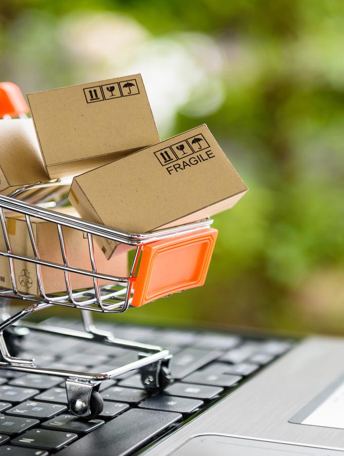 Miniature scale shopping cart with shipping boxes in it on top of a laptop keyboard