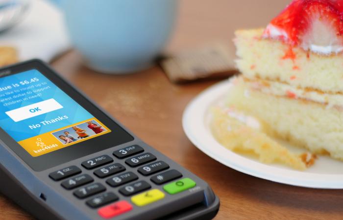 Verifone's P400 PIN pad on a table next to a cup of coffee and a slice of strawberry shortcake