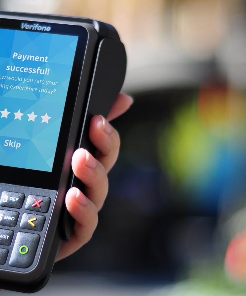 Verifone V400m portable payment device held in hand with blurred outdoor background