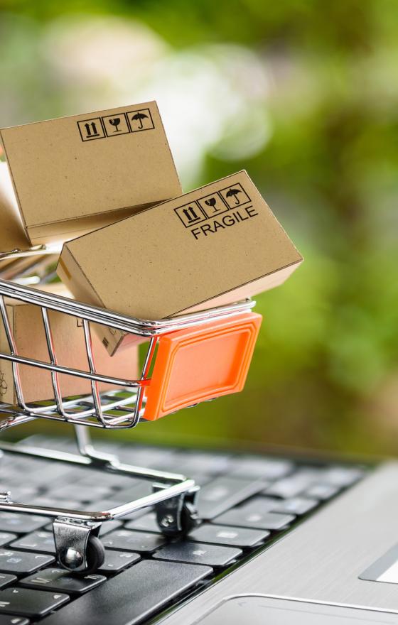 Miniature scale shopping cart with shipping boxes in it on top of a laptop keyboard